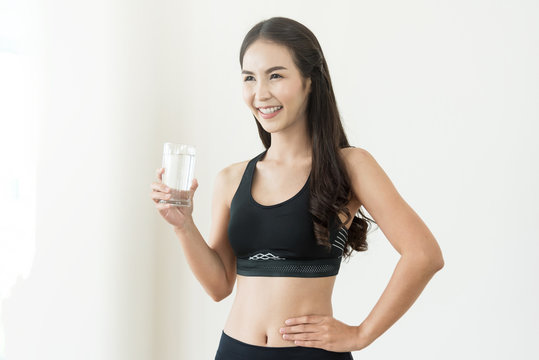 Happiness Young Asian Woman in black sportswear holding glass of water on white isolated background. Healthy, Diet, Beauty, smiling.