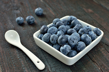 Blueberry fruit on wood background. Forest fruit in white idaeus and spoon. Delicious fresh berries.