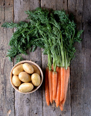 Organic potatoes and carrots with a tops on an old wooden background.