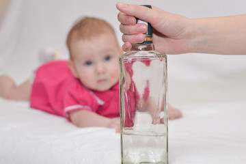Female hand holds a bottle of vodka on the background of a toddler lying on a white background. The...