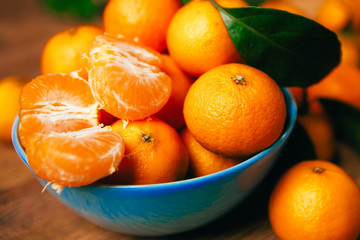many fresh mandarin oranges in  blue bowl, standing on a wooden table 