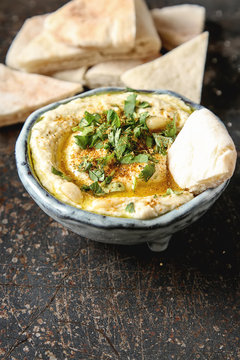 Classic hummus with herbs, olive oil in a vintage ceramic bowl and pita bread. Traditional Middle Eastern cuisine. Dark background.