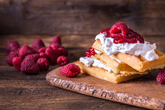 Belgian waffles with raspberries and double cream on rustic table.