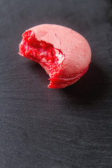 Traditional French sweets. A piece of red macaroon. Black stone background.