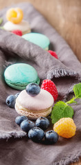 Traditional French sweets. Assorted colorful macaroons with mint green, white and red raspberries, blueberries. Dark wood background.