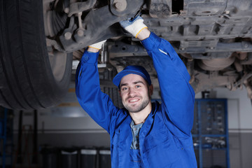 Young mechanic fixing wheel under car in  service