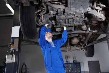 Young mechanic fixing wheel under car in  service
