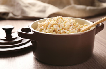 Modern ceramic saucepan full of boiled brown rice on wooden table