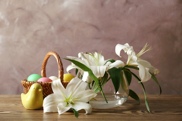 Beautiful Easter composition with lilies and eggs in wicker basket on wooden table
