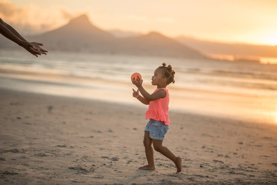 Little girl holding ball at the beach at sunset