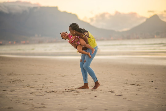 Mother playing with her daughter on the beach at sunset