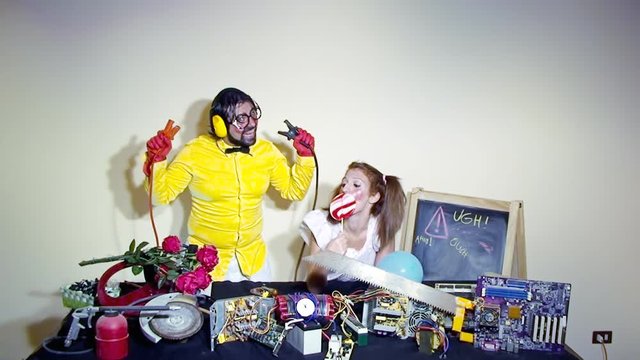 A weird salesman fooling with a pair of jumper cables, together with his female assistant. Close-up shot. Funny comedy foolish characters.
