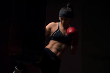 A boxer girl wearing red gloves and a bandana is hitting the bag