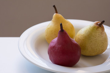 against the light view of a closeup of three organic pears in a white plate