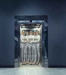 Clones of young women in silver futuristic costume standing in the elevator.