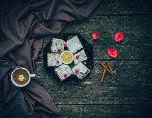 Lemon pie on a plate with alcoholic cherries and fresh tea with cinnamon on wooden background Board with flowers.