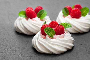 Mini  Pavlova meringue nests with raspberries and mint on black stone background
