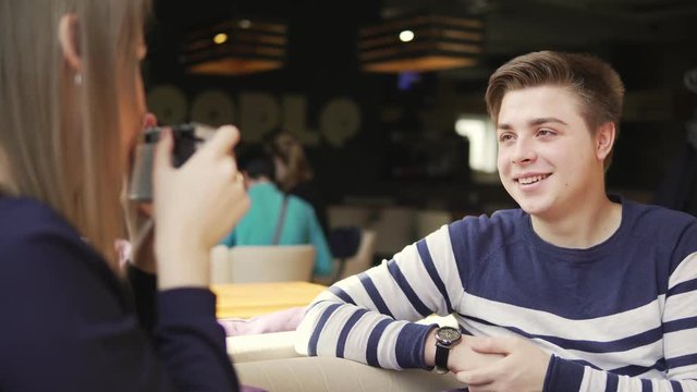 Young couple having fun in cafe. Young woman taking pictures using photo camera, man posing for his girlfriend. Shot in 4k