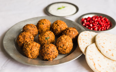Crispy falafel and Arab pita bread with pomegranate seeds and white sour cream sauce against white background. Selective focus.