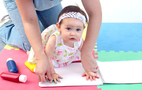 Baby painting her print hands in a notebook