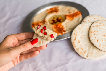 Woman with beautiful hands eating pita bread with hummus and pomegranate seeds. Healthy food, fitness, and sport diet concept.