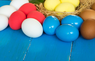 Fototapeta na wymiar Colored eggs in nest on rustic blue wooden background, selective focus image. Happy Easter Card - space for text 