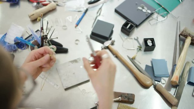  Overhead view looking down jewelry designer at workbench with tools, materials & jewelry items. 