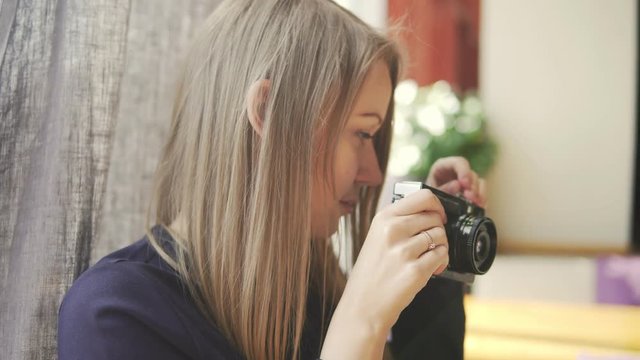 Young girl taking photos with vintage camera in cafe, having fun. Shot in 4k