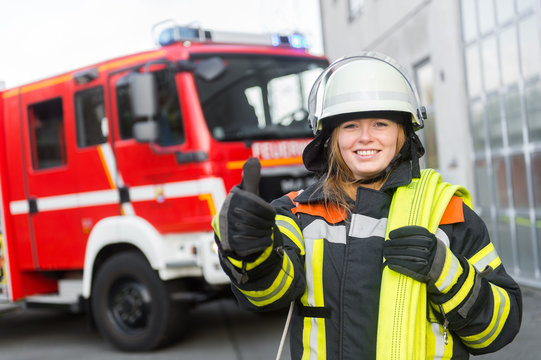 Feuerwehrfrau steht vor Löschfahrzeug und hält Daumen hoch