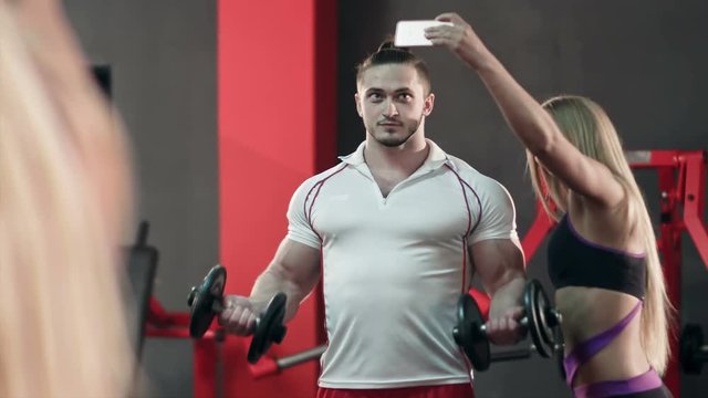 Sporty woman taking selfie with strong man working out in the gym