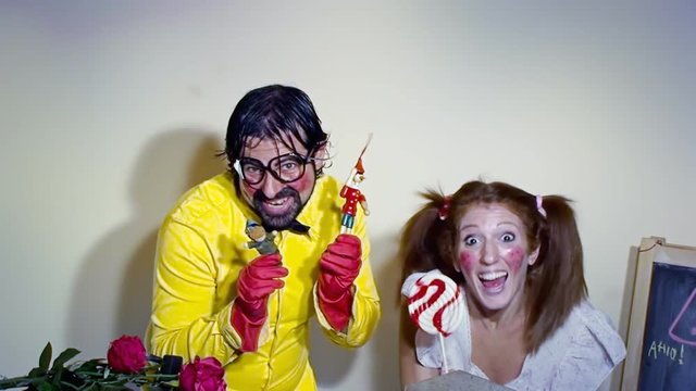 A weird salesman moving a Pinocchio toy, together with his female assistant licking a lollipop. Close-up shot. Funny comedy foolish characters.
