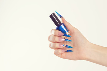 Nail Polish. Art Manicure. Modern style blue Nail Polish. Beauty hands holding blue bottle. Stylish Colorful stiletto Nails isolated white background