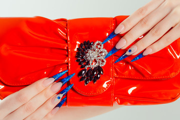 Nail Polish. Art Manicure. Modern style blue Nail Polish. Beauty hands holding red bag clutch with...