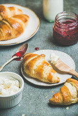 Breakfast concept. Freshly baked croissants with raspberry jam, ricotta cheese and milk in bottle over grey concrete background, selective focus