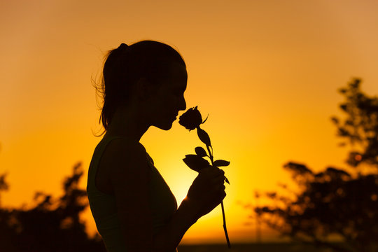 Silhouette of woman smelling a rose flower. 