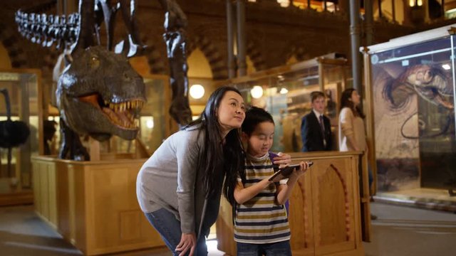  Mother & son in museum, standing by dinosaur skeleton & looking at computer