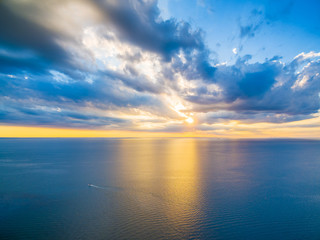 Naklejka na ściany i meble Aerial panoramic view of lonely boat sailing across ocean at beautiful sunset. Beautiful glowing yellow light reflecting in blue bay waters