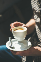 Cup of coffee cappuccino in man's hands in street cafe under sunlight, copy space