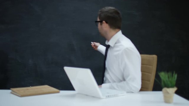 Businessman with laptop moving his hand as if underlining a word on chalkboard