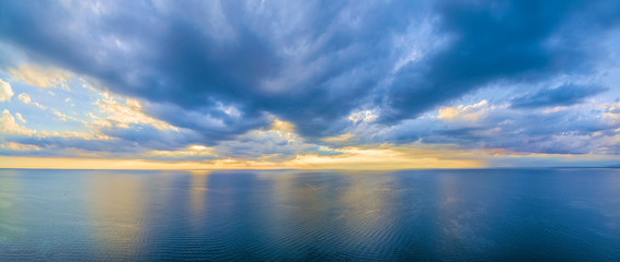 Naklejka na ściany i meble Aerial panoramic view of ocean water and beautiful blue skies at glowing yellow sunset. Nothing but water and clouds