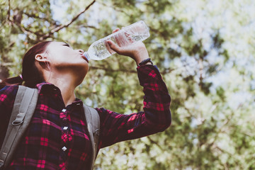 young asian woman drinking water in the forest. Hiking at summertime.