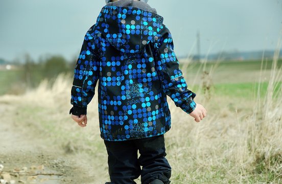Boy wearing softshell jacket and walking along a dirt road in chilly and windy weather. Child concept.