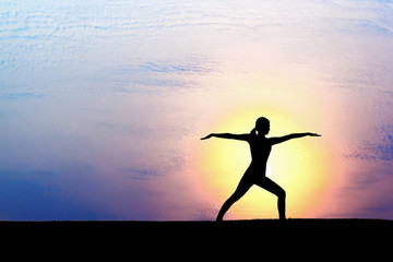 Woman practicing warrior yoga pose outdoors over sunset sky background.