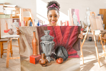 Portrait of a young african ethnicity student standing with paintings at the university studio