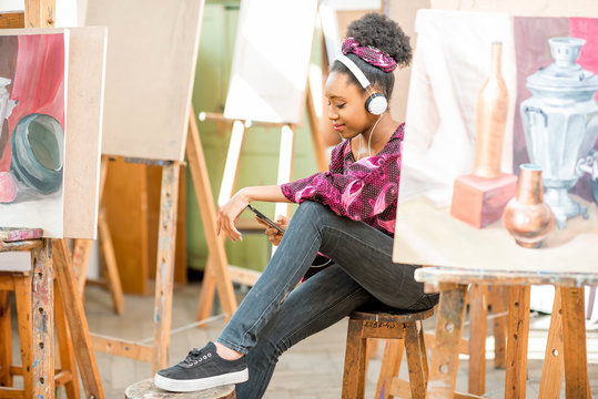 Portrait of a young african ethnicity student sitting with phone during the break at the studio for painting