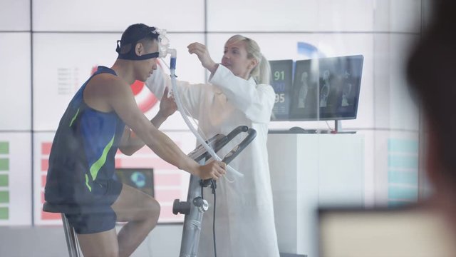  Sport scientist in white coat assessing fitness of man on exercise bike. 