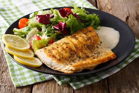 Grilled char fillet with mixed salad and sauce on a plate close-up. horizontal