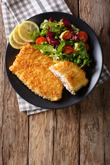 Fried fish fillet in breading and fresh vegetable salad close-up. Vertical top view