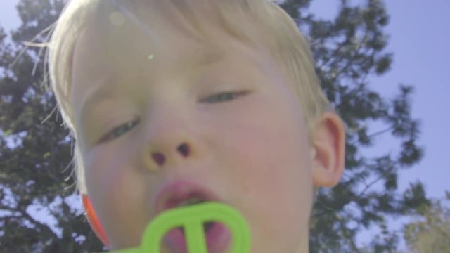 Funny boy tries to blow a soap bubble with a wand as the camera pushes in for a tight close up on his face