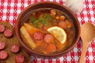 saltwort russian beef, pork and sausage soup solyanka with lemon, salami in plate on red cloth